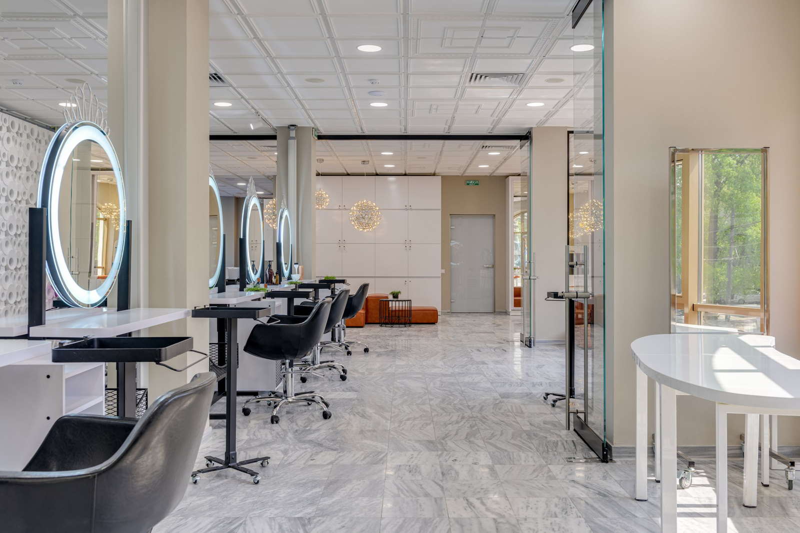 A row of lit oval mirrors and empty styling chairs down a bright salon floor