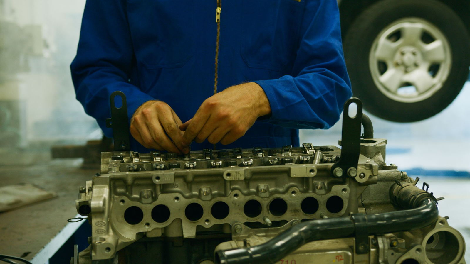 Gloved hands working across the valve seats of a cylinder head on a bench