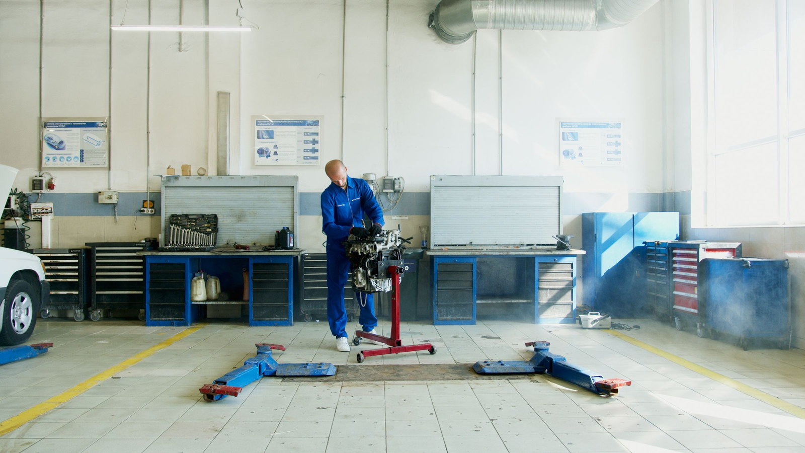 A technician alone in a bright workshop, working at an engine on a stand between two benches