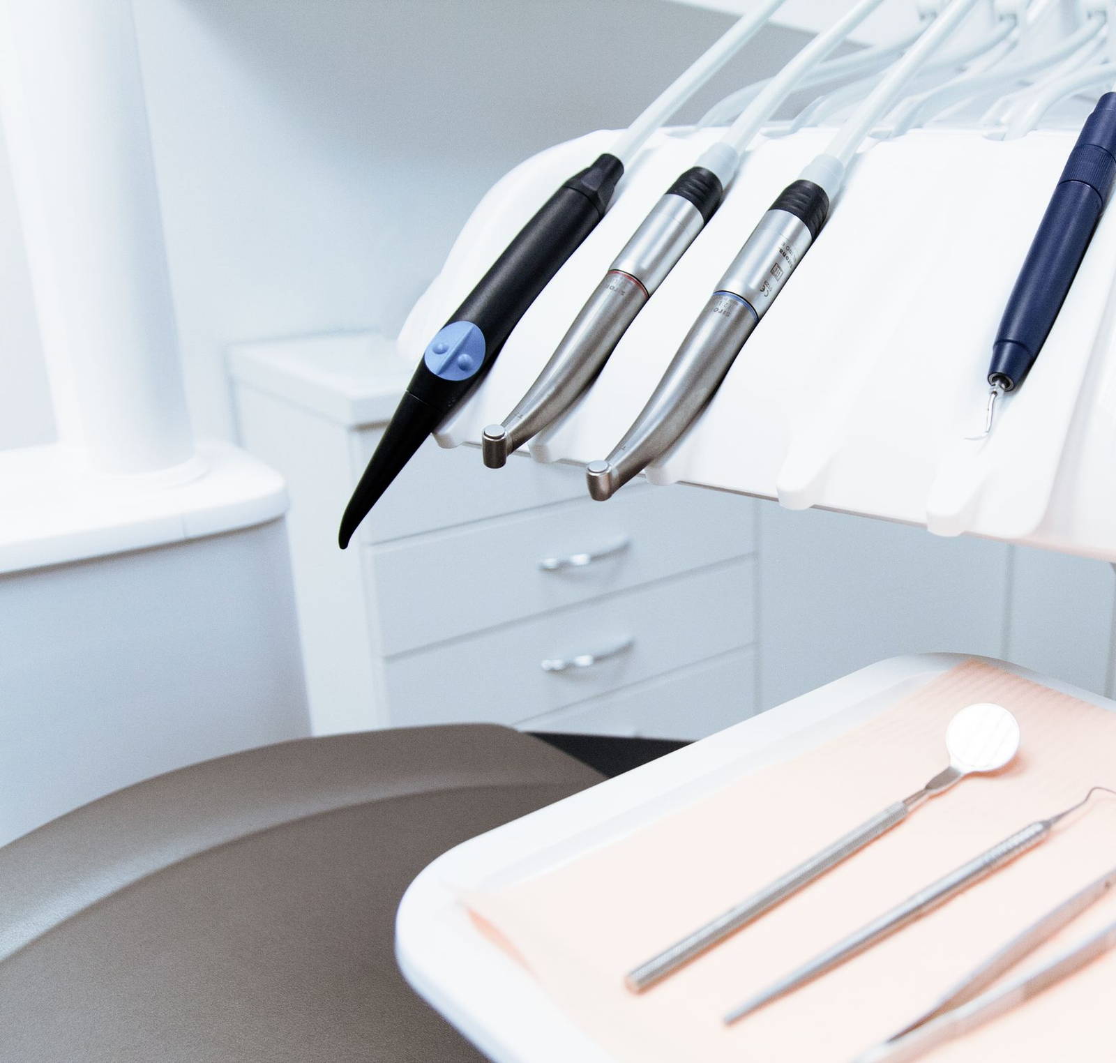 Four handpieces racked on the delivery arm above a tray of mirror and probes