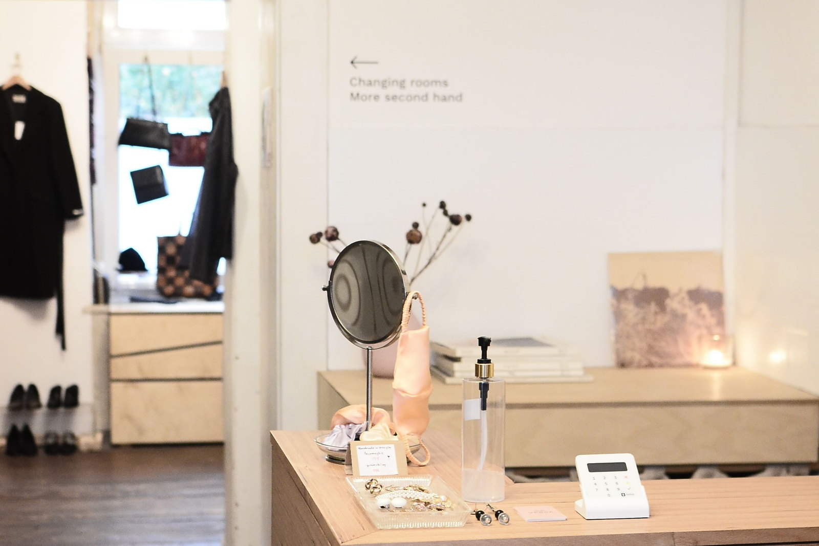 A plywood shop counter with a mirror, card reader and jewellery tray, changing rooms through the doorway behind