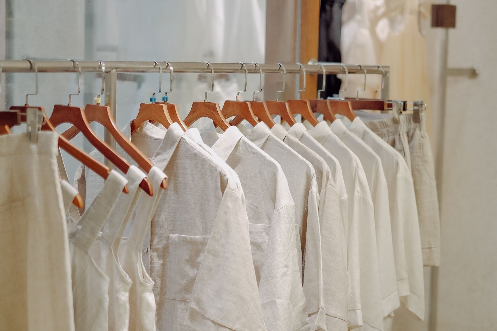 A rail of undyed linen shirts on timber hangers against a plain wall