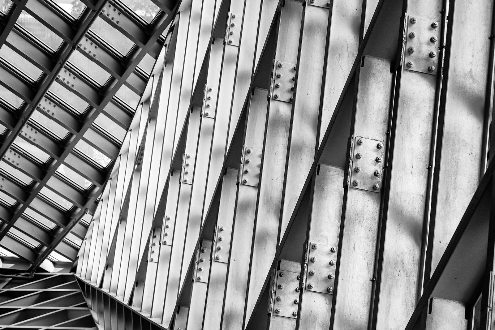 Steel trusses and bolted splice plates against concrete, shot from below, black and white