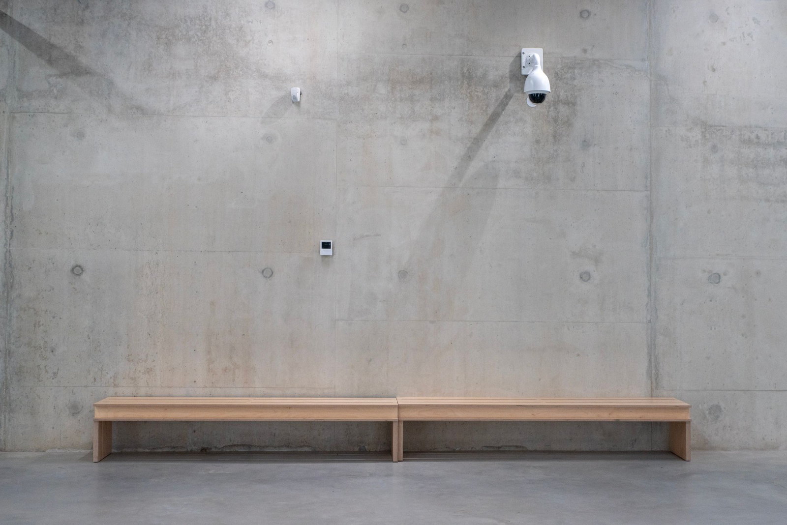 A timber bench against a bare concrete wall, a single camera mounted above it