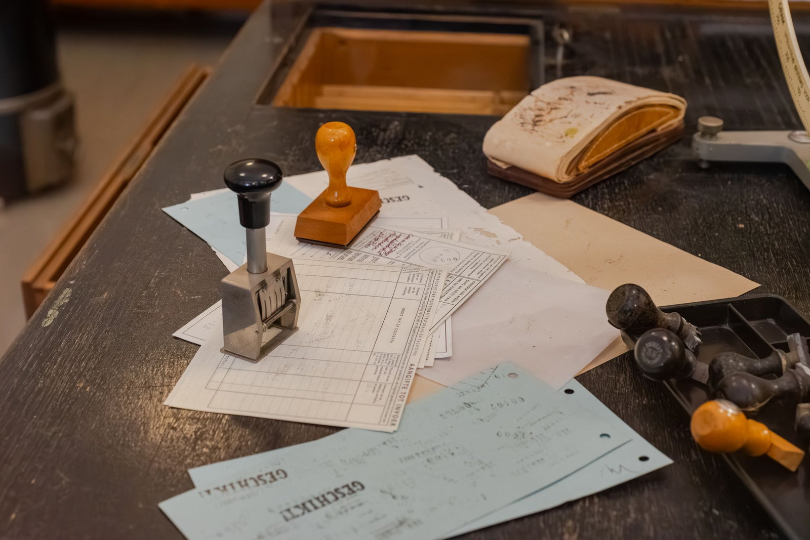 A clerk’s desk of official forms with a numbering stamp, a wooden hand stamp and a tray of others